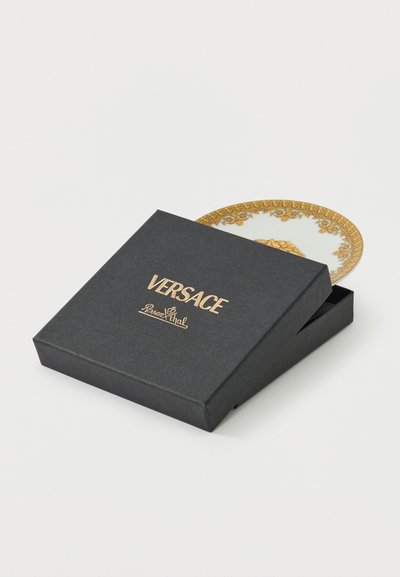 Μαύρο κουτί Versace Rosenthal μερικώς ανοιχτό, αποκαλύπτοντας το λευκό και χρυσό περίτεχνο χείλος ενός πιάτου στο εσωτερικό, σε λευκό φόντο.