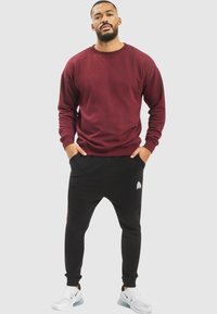 Burgundy crewneck sweatshirt paired with black tapered joggers. Joggers feature a side pocket and logo detail. White sneakers complete the look.