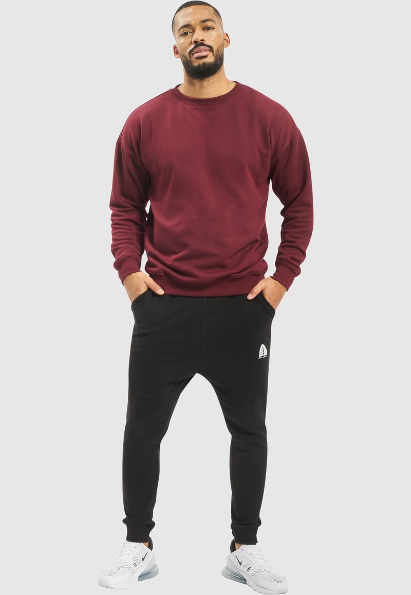 Burgundy crewneck sweatshirt paired with black tapered joggers. Joggers feature a side pocket and logo detail. White sneakers complete the look.