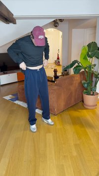 Tamne tamne plave trenirke s elastičnim pojasom, uparene s crnom majicom dugih rukava i tamnocrvenom kapom, smještene u dnevnom boravku.