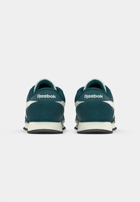 Par tenisica Reebok u tirkiznoj i bijeloj boji prikazanih sa stražnje strane na jednostavnoj svijetlosivoj pozadini.