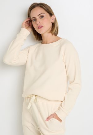 Haut long en maille gaufrée beige avec un col rond et des poignets côtelés, associé à un bas à taille drawstring assorti.