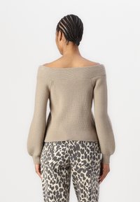 Beige off-shoulder knitted sweater with ribbed texture and voluminous sleeves, paired with gray and beige leopard print pants.