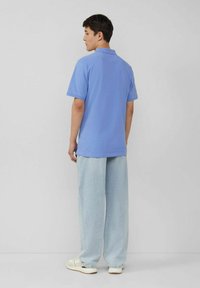 Helles blaues Poloshirt kombiniert mit hellblauen, weit geschnittenen Jeans. Baumwollmaterial, kurze Ärmel und ein einfaches, klassisches Design. Legere Schuhe.