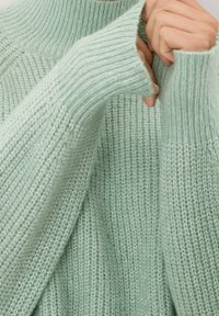 Maglione a maglia di un verde menta chiaro con un collo alto a coste e maniche ampie. La texture è morbida e leggermente spessa, caratterizzata da una vestibilità rilassata.