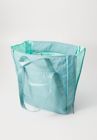 Lichtblauw Nike draagtas met dubbele handvatten, voorzak en een open bovenkant, die een ruime binnenkant en het gestikte swoosh-logo toont.