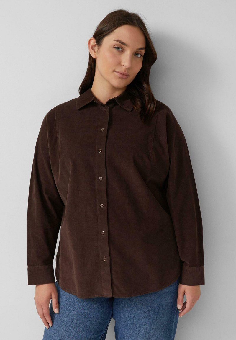 Bruine corduroyButton-up shirt met een kraag, met lange mouwen en een losse pasvorm, gecombineerd met blauwe denim jeans. Soepele textuur, eenvoudig ontwerp.