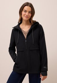 Zwarte softshell jacket met een ritssluiting aan de voorkant, verstelbare capuchon en twee voorzakken. Voorzien van elastische manchetten en een logo op de mouw.