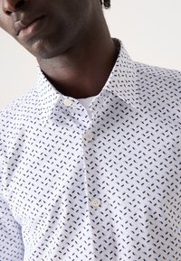 Hvit skjorte med små marineblå og lyseblå geometriske mønstre, button-down krage og knapper foran.
