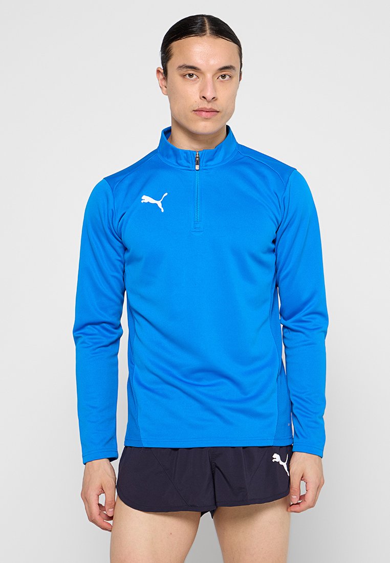 Camiseta deportiva de manga larga en azul brillante, con cuello de cremallera de un cuarto y logotipo de Puma en blanco en el lado izquierdo del pecho. Tela suave y ligera.