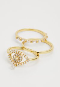 Ensemble de bagues en ton or comprenant trois bandes : une avec des pierres claires, une avec un design décoratif en forme d'œil orné de perles et d'un charme en goutte.