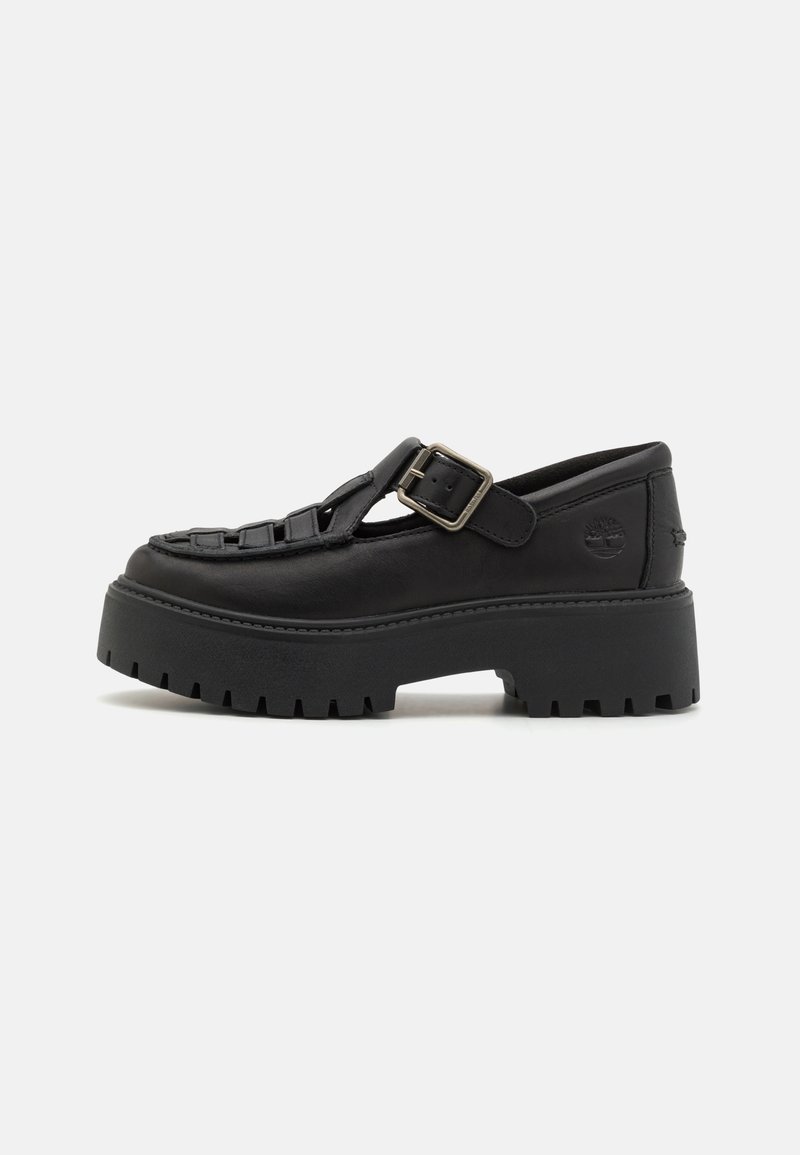 Chaussure à plateforme en cuir noir avec semelle épaisse à crampons, design ajouré et bride ajustable à boucle métallique sur le dessus.