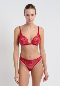 Sujetador de encaje rojo y tanga a juego con delicados patrones florales, tirantes finos y una textura suave, que enfatizan los detalles intrincados.