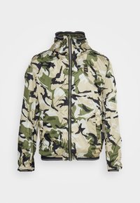 Chaqueta de camuflaje en beige, verde y negro. Cuenta con un alto cuello, cremallera frontal y puños elásticos. Tejido ligero y texturizado.