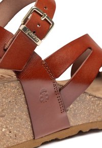 Sandal in pelle marrone con fibbia regolabile, suola in sughero e design a ritaglio. Dettaglio notevole include il logo impresso sul pannello laterale.