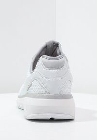 White athletic shoe with a textured mesh design, smooth leather accents, and a cushioned grey collar. Thick white sole for support.