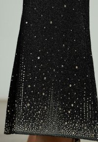 Vestido negro con una textura brillante y acentos de piedras preciosas transparentes, creando un efecto de degradado de adornos densos a escasos.