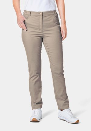 Pantalons beiges avec une fermeture à bouton à l'avant, coupe slim, et poches latérales, associés à des chaussures de sport blanches et un haut blanc.