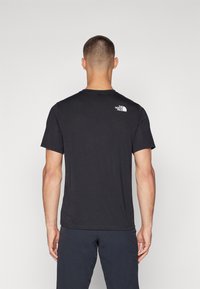 Svart bomull T-skjorte med rund hals, korte ermer og hvit The North Face-logo på øvre rygg. Myk tekstur.