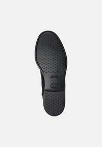 Suela de zapato de goma negra con una superficie texturizada que presenta pequeños puntos, marca grabada y un borde redondeado para un diseño flexible.