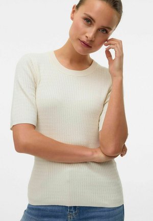 Haut en tricot crème à manches courtes avec une texture côtelée et un col rond. Design ajusté, associé à un jean en denim bleu.