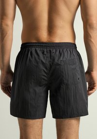Černé plavecké šortky s elastickým pasem, zadní kapsou a texturovanou tkaninou. Vyznačují se jednoduchým a funkčním designem.