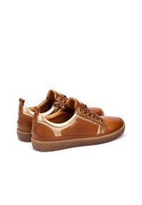 Baskets en cuir brun avec des accents métalliques dorés, bout rond et design à lacets. Semelle en caoutchouc texturé avec des détails sur le côté.