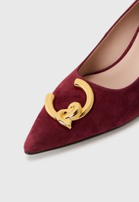 Décolleté in suede mauve con punta affilata, caratterizzato da una brillante fibbia decorativa in tonalità oro e una morbida fodera interna.