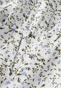 Kukkainen paita, jossa on valkoinen kangas vihreillä ja vaaleansinillä kukkakuoseilla, pieni etunappikiinnitys ja V-muotoinen pääntie.