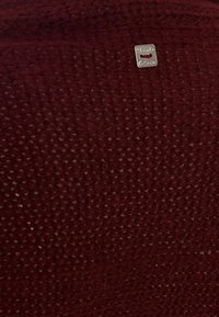 Tessuto lavorato a maglia bordeaux con un pattern testurizzato e un piccolo tag argentato con il nome del marchio.