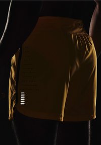Los pantalones cortos deportivos amarillos cuentan con una superficie texturizada, aberturas laterales para mayor movilidad y un patrón de rayas vertical distintivo con acentos reflectantes.