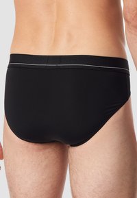 Slip da bagno neri realizzati in materiale elastico, con una texture liscia, design a vita bassa e un bordo argentato a contrasto lungo l'elastico in vita.