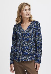 Blusa a maniche lunghe con scollo a V, realizzata in tessuto leggero, con uno sfondo blu scuro decorato da motivi floreali multicolori.
