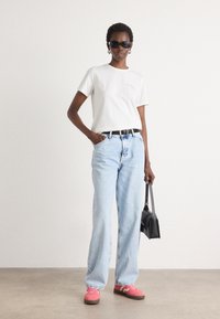 T-shirt in cotone bianco, jeans a gamba dritta blu chiaro, sneakers rosa con suola nera e borsa nera. Gli accessori includono occhiali da sole scuri.