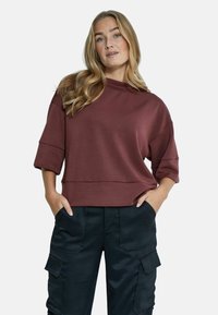 Burgundy cropped huppari, jossa on korkea kaulus, väljät hihat ja pehmeä tekstuuri; yhdistetty mustiin cargo-housuihin, joissa on sivutaskut.
