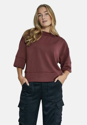 Burgundy cropped huppari, jossa on korkea kaulus, väljät hihat ja pehmeä tekstuuri; yhdistetty mustiin cargo-housuihin, joissa on sivutaskut.