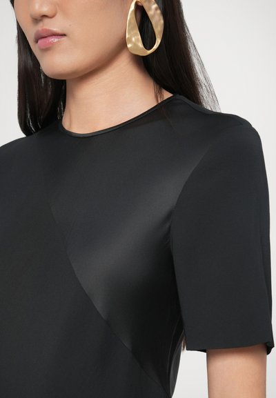 Fekete felső, sima, elegáns anyagból, rövid ujjakkal és kerek nyakkivágással. Aranyszínű, texturált karika fülbevalók erőteljes hangsúlyt adnak a megjelenésnek.