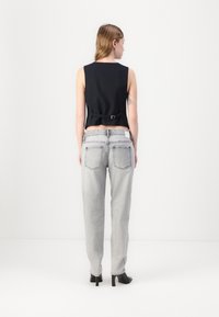 Top senza maniche nero a coste con dettaglio della cintura in vita, abbinato a jeans grigi chiari a gamba dritta. Scarpe nere con tacco completano il look.