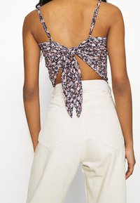 Blommönstrad tygcrop top med knytning bak, med tunna axelband. Kombinerad med högmidjade beige byxor och en mjuk textur.