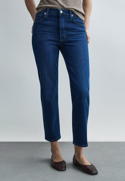 Μπλε τζιν υφάσματος denim με ψηλή μέση, κανονική γραμμή παντελονιού και πέντε τσέπες. Χωρίς εμφανή φθορές ή διακοσμήσεις, συνδυασμένο με σκούρα μπαλαρίνια.