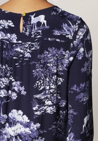 Blusa navy con un design floreale e a stampa animale in tonalità viola. Caratterizzata da una schiena a chiave e da una texture di tessuto morbido.