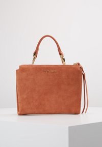 Torebka z zamszu w kolorze brzoskwiniowym o strukturalnym kształcie, z górnym uchwytem, złotymi akcentami i długim detalem w postaci frędzla.