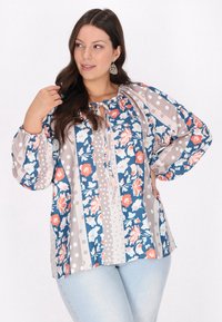 Blomstret bluse med blå og beige striber, prydet med prikker. Tekstureret stof, løs pasform og snor i halsen. Lange, rynkede ærmer.