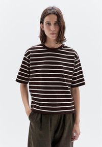 Brunstribet t-shirt med korte ærmer og rund halsudskæring. Båret med løse, mørke bukser. Stoffet ser blødt ud, og striberne er jævnt fordelt.