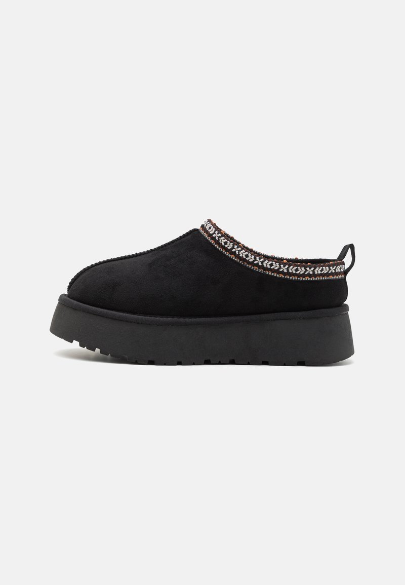 Scarpa slip-on in suede nero con suola in gomma nera spessa e una finitura decorativa a motivo attorno al collo. Presenta un tassello sul retro.