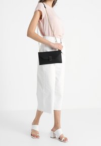 Svart läder crossover-väska med en strukturerad design, som har en rektangulär klaff, silvriga detaljer och en avtagbar kedjestrag.