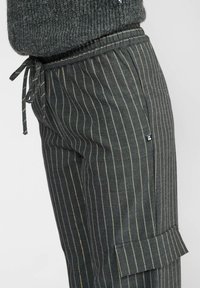 Gros plan sur un pantalon à rayures noires avec une taille élastique et un cordon de serrage, associé à un pull en maille sombre.