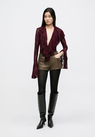 Bordowa koronkowa bluzka z falbanami i długimi rękawami, zestawiona z oliwkowozielonymi szortami, czarnymi rajstopami oraz czarnymi kozakami na obcasie do kolan.