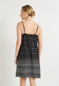 Vestido negro sin mangas con tejido estampado que presenta un diseño geométrico blanco y un dobladillo acampanado, llegando a mitad de la pantorrilla.