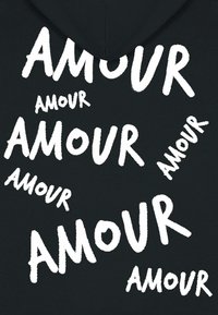 Felpa nera con cappuccio che presenta testo bianco in diverse dimensioni che scrive "AMOUR" in uno stile audace e scritto a mano, con una texture morbida.
